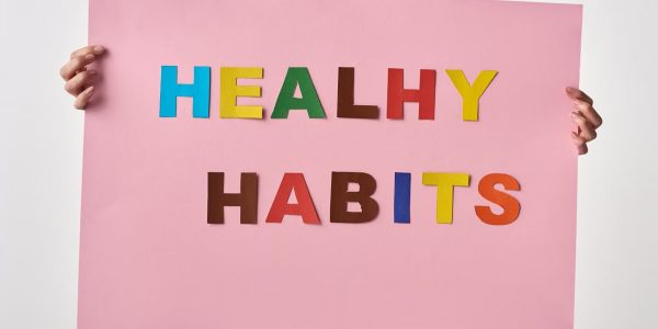 A woman holds a pink poster with colorful letters spelling 'HEALTHY HABITS'.