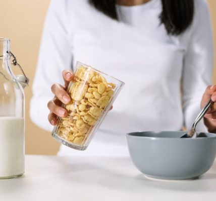 Person pouring cereal into a bowl with a bottle of milk nearby, ready for breakfast.