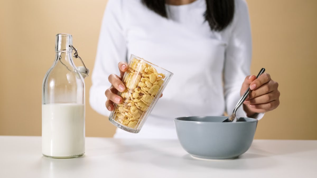 Person pouring cereal into a bowl with a bottle of milk nearby, ready for breakfast.